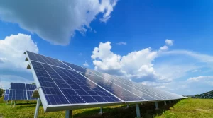 Paineis solares fotovoltaicos instalados em campo aberto, com céu azul e nuvens ao fundo, mostrando geração de energia renovável por meio da luz do sol.